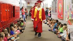 a man in red and yellow graduation gown walking down a hallway with children sitting on the floor