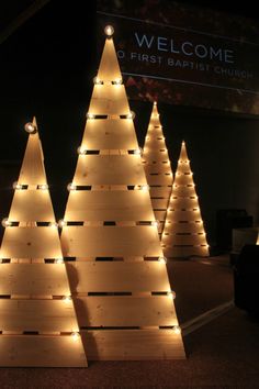 lighted wooden christmas trees in front of a welcome sign