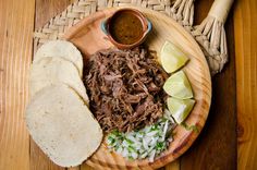 a wooden plate topped with meat and vegetables next to tortilla bread on top of a table