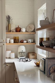 a kitchen with white counter tops and shelves filled with plates, cups, bowls and utensils