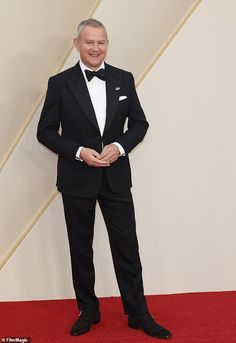 an older man in a tuxedo poses on the red carpet