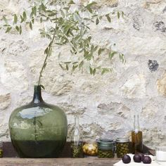 a green vase sitting on top of a wooden table next to jars filled with olives