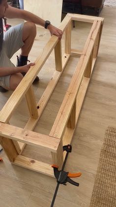 a man kneeling down on the floor working on a wooden frame