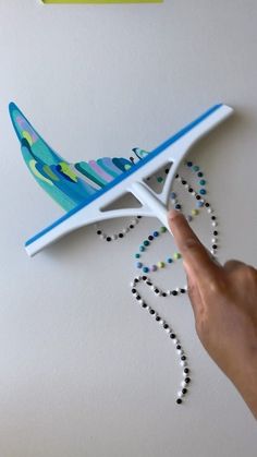 a hand is pointing at a blue and white airplane on the wall with beaded necklaces