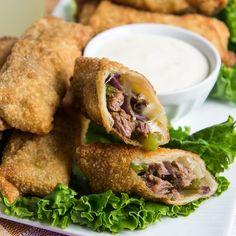 an egg roll with meat and lettuce is on a plate next to dipping sauce