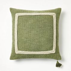 a green and white pillow with a tasselled square on the front, sitting on a white surface