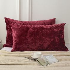 two red velvet pillows sitting on top of a bed next to a white nightstand and lamp