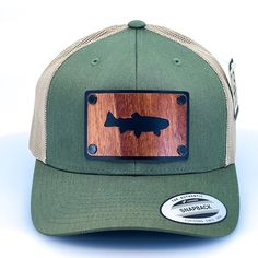 Introducing our stylish and durable olive green and khaki trucker cap, perfect for any outdoor adventure. The hat features a special patch made exclusively in our shop in Missoula, Montana. The patch is made of high-quality mahogany veneer and has been cut out in the shape of a trout, laminated to a black anodized aluminum plate, and secured with black rivets. The design on the mahogany veneer adds a unique touch to the hat with its intricate details and natural wood grain. The cap features a br Green 5-panel Trucker Hat For Outdoor, Fishing Hats For Men, Trucker Snapback Hat For Fishing, Military Style Khaki Snapback Trucker Hat, Military Style Camouflage Trucker Hat For Outdoor, Manly Man, Green Military Snapback Trucker Hat, Missoula Montana, Hat Patches