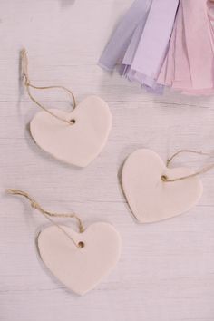 three ceramic hearts hanging from twine on white wooden table with pink and purple ruffles