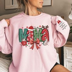 Make this holiday season extra special with our Custom Mama Claus Sweatshirt and Hoodie! This personalized Christmas sweatshirt allows you to add your children's names on the sleeves, making it a unique and thoughtful gift for moms, nana,gigi or grandmas. Whether you're getting cozy at home or heading out for festive gatherings, this custom sweatshirt adds a personal touch to the holiday spirit. It's the perfect Christmas gift for moms or grandmas who love to show off their family in style. Cele Mama Christmas Sweatshirt, Christmas Graphic Print Long Sleeve Hoodie, Christmas Long Sleeve Cotton Hoodie, Christmas Long Sleeve Tops With Cozy Fit, Letter Print Sweatshirt Winter Gift, Pink Tops As Winter Gifts, Christmas Hoodie With Letter Print And Crew Neck, Christmas Cotton Hoodie With Letter Print, Christmas Cotton Hoodie With Crew Neck