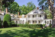 a large white house sitting in the middle of a lush green field next to trees