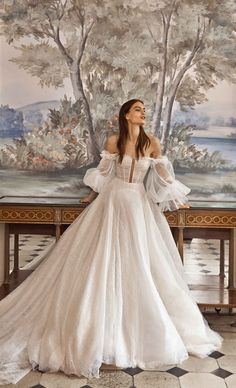 a woman standing in front of a painting wearing a white dress