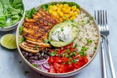 a bowl filled with chicken, rice, beans and avocado next to a salad