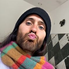 a man with long hair and a beard wearing a multicolored scarf is making a funny face