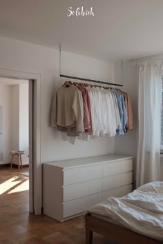 a white bedroom with clothes hanging on the rack