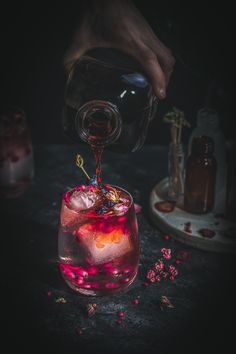 a person pours some liquid into a glass filled with ice and raspberries