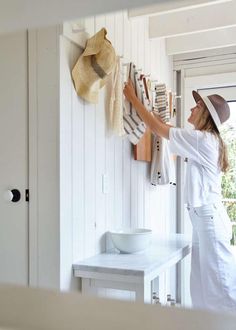 a woman in white is hanging clothes on the wall next to a bowl and hat