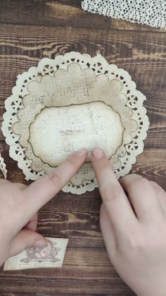 two hands are pointing at an object on a wooden table with doily around it