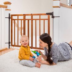 a woman playing with a baby on the floor in front of a wooden gate and stairs