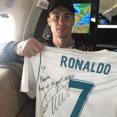 a man holding up a signed shirt in front of a tv screen on an airplane