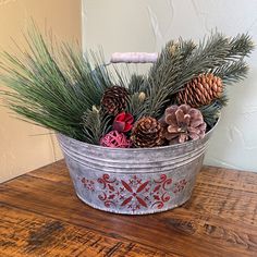 a metal bucket filled with pine cones and evergreen branches on top of a wooden table