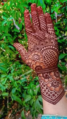 a hand with henna on it in front of some trees and bushes at the park