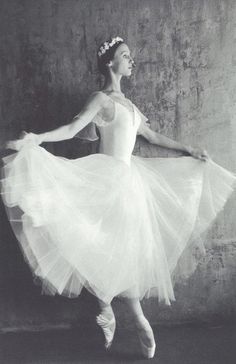 a black and white photo of a ballerina wearing a tulle skirt in front of a wall