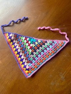 a crocheted triangle on a wooden table with a pink string attached to it