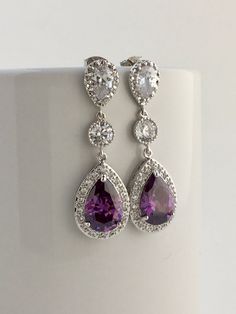 Luxury purple amethyst cubic zirconia bridal teardrop earrings in rhodium plated brass setting. I've created these luxurious earrings using a large teardrop with pear cut purple amethyst cubic zirconia center surrounded by tiny round zirconia crystals. Teardrop dangles from a clear cubic zirconia ear stud and a round cubic zirconia connector. Total length of the earring is 4.6 cms. For matching necklace click: https://www.etsy.com/listing/465785454/purple-amethyst-cubic-zirconia-bridal?ref=listi Luxurious Earrings, Purple Drop Earrings, Drop Earrings Wedding, Luxury Purple, Purple Dangle Earrings, Teardrop Bridal Earrings, Black Crystal Earrings, Pink Pearl Earrings, Lavender Earrings