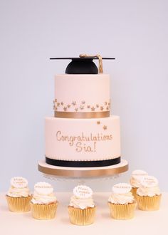 a three tiered cake with cupcakes on the side and graduation cap on top