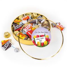 a round tin filled with assorted chocolates and candy bar wrappers next to it