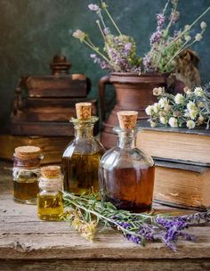 three bottles filled with different types of oils next to some flowers and books on a table