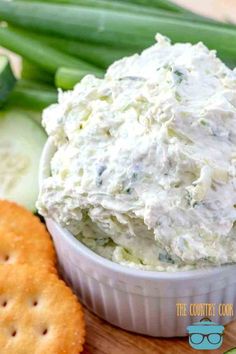 a white bowl filled with dip surrounded by crackers and cucumbers