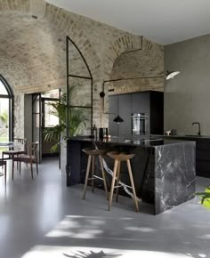 an open kitchen and dining area with marble counter tops, bar stools, and brick walls