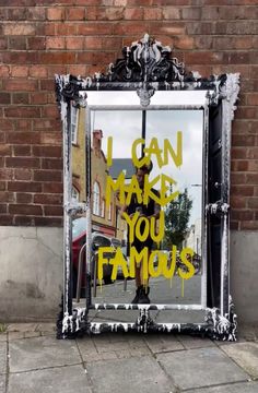 a mirror sitting on the side of a street next to a brick wall with graffiti written on it