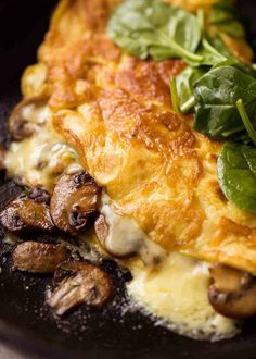 an omelet with mushrooms and spinach leaves on top is served in a black plate