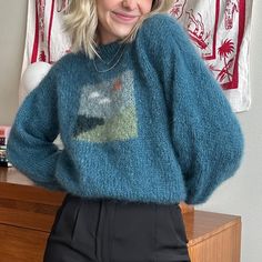 a woman wearing a blue sweater and black pants standing in front of a wooden dresser