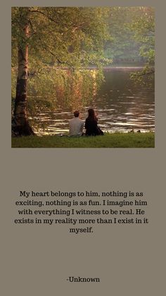 two people sitting next to each other on the grass near water with trees in the background