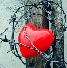 a red heart is attached to a barbed wire fence