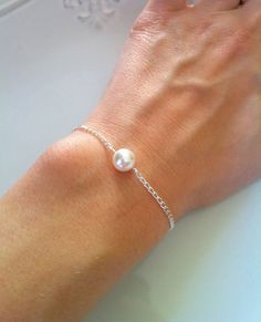 a woman's hand wearing a bracelet with a pearl on it