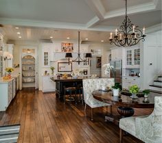 a large open kitchen and dining room with wood floors, white cabinets and chandelier