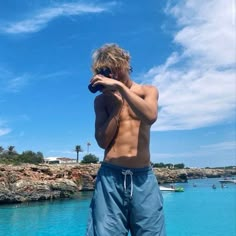 a shirtless man standing on the edge of a boat looking at his cell phone