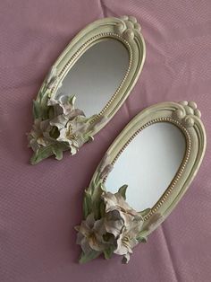 two mirrors with flowers on them sitting on a pink surface next to a purple sheet