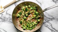 a pan filled with noodles and broccoli on top of a marble countertop