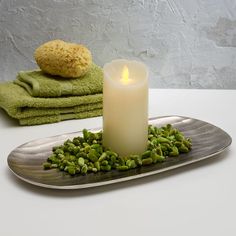 a lit candle sitting on top of a metal plate next to towels and green towel