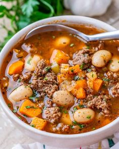 a white bowl filled with meat and vegetable soup on top of a table next to some parsley