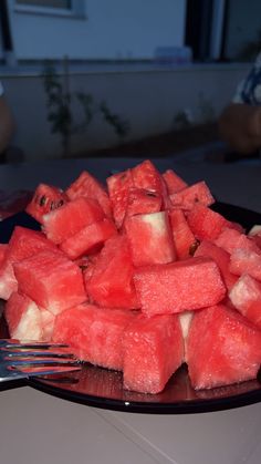 a plate full of watermelon cut into cubes with a fork in it