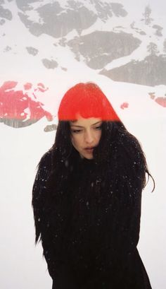 a woman standing in the snow wearing a red hat