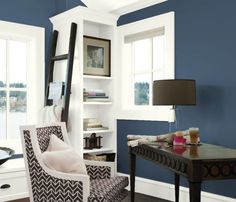 a living room with blue walls and white trim on the ceiling, along with a chair that is upholstered in front of a bookcase