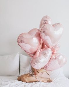 a woman laying on top of a bed covered in pink heart shaped balloons